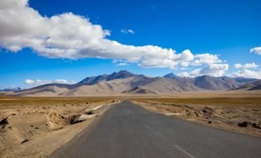 A breathtaking view of the desert road leading to mountains in Ladakh, India under a clear blue sky.