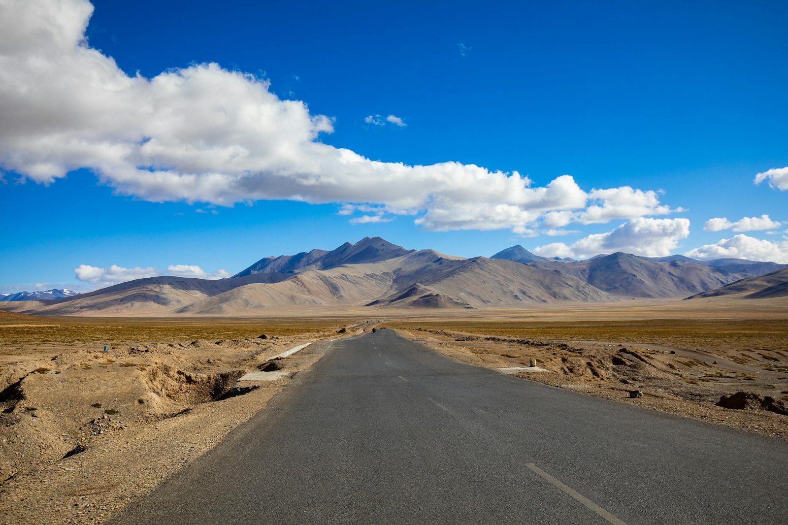 A breathtaking view of the desert road leading to mountains in Ladakh, India under a clear blue sky.
