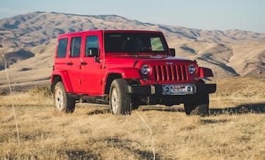 A striking red Jeep Wrangler parked in a vast, desert-like landscape under a clear sky.