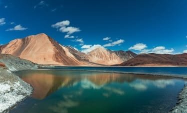Beautiful panorama of Pangong Lake with majestic Himalayan mountains under a clear blue sky.
