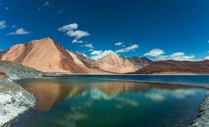 Beautiful panorama of Pangong Lake with majestic Himalayan mountains under a clear blue sky.