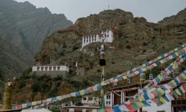 Colorful many flags hanging on street near ancient Hemis monastery with pillars located in mountainous terrain in India against gray sky