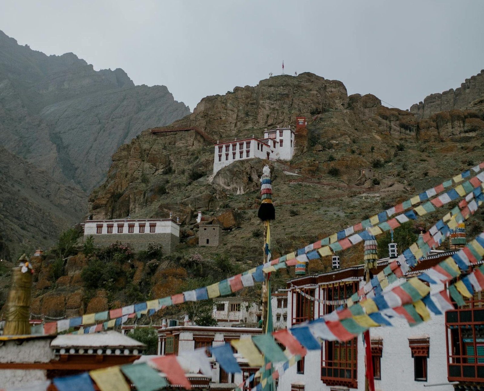 Colorful many flags hanging on street near ancient Hemis monastery with pillars located in mountainous terrain in India against gray sky
