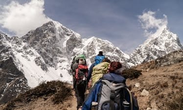 Group of hikers trekking on a sunny day with snow-capped mountains in the background. Outdoor adventure scene.
