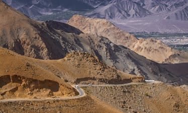 Winding road through majestic mountains in Ladakh, India, under a clear sky.